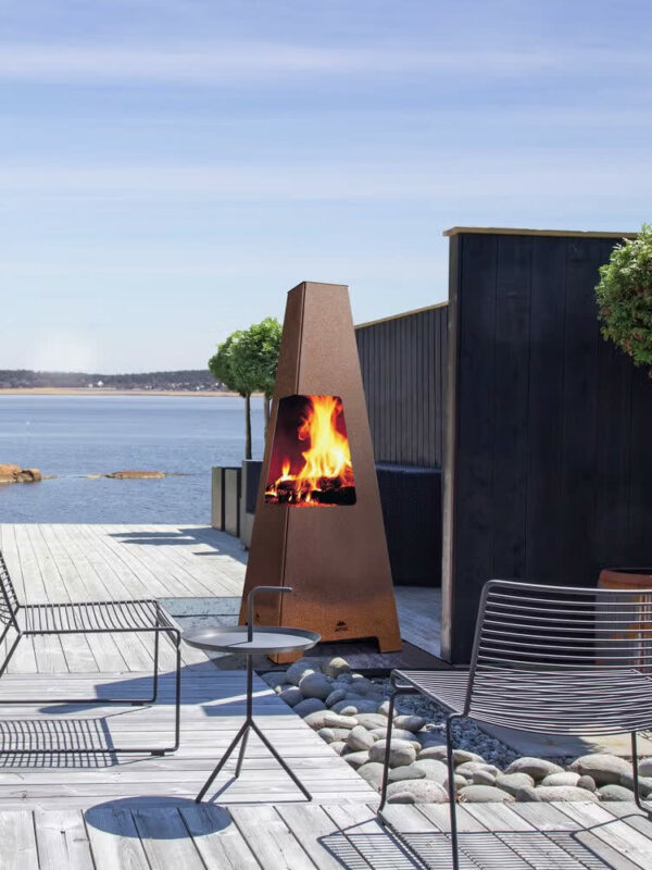 Foyer d'extérieur Jøtul TERRAZZA XL en acier Corten, sur une terrasse en bois avec mobilier d'extérieur